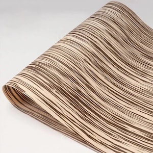 Op de afbeelding: Een opgerolde decoratieve papieren vel met een herhalend patroon van donkerbruine, golvende lijnen op een lichtbeige achtergrond. Het papier heeft een houtnerf-uiterlijk, geschikt voor knutsel- en designprojecten.