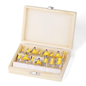 May include: A wooden box set containing a variety of yellow and silver router bits. The bits are arranged neatly inside the open box, which has a light-colored interior and a silver clasp. The set is designed for woodworking and includes various bit profiles.