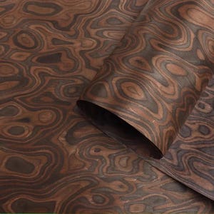 May include: Close-up of a sheet of wood veneer with a swirling, organic pattern. The veneer features shades of brown and dark grey, creating a natural, textured appearance. The sheet is partially rolled, revealing the underside.