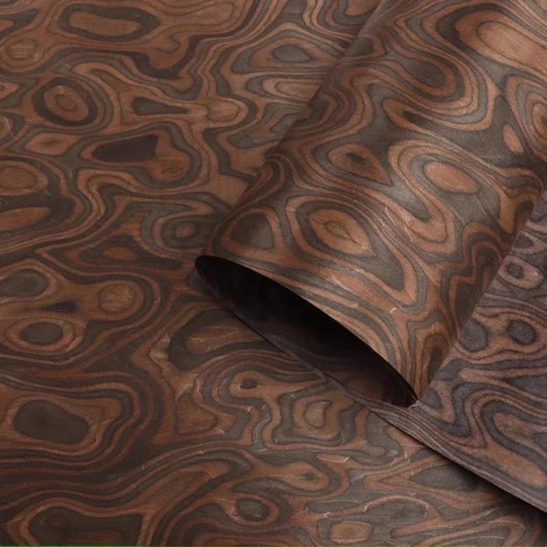 May include: Close-up of a sheet of wood veneer with a swirling, organic pattern. The veneer features shades of brown and dark grey, creating a natural, textured appearance. The sheet is partially rolled, revealing the underside.