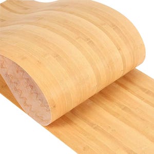 Puede incluir: Un rollo de chapa de bambú marrón claro, parcialmente desenrollado. La chapa tiene un patrón de vetas de madera natural con líneas verticales. La parte inferior tiene un respaldo claro y marrón con dibujos.