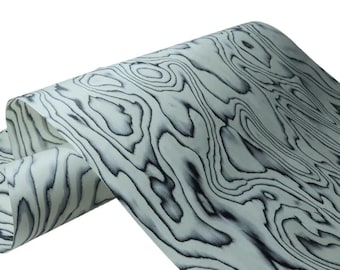 May include: A roll of flexible material featuring a high-contrast black and white wood grain pattern. The surface displays organic, flowing lines and concentric shapes that mimic the natural texture of timber, presented in a folded, layered form.