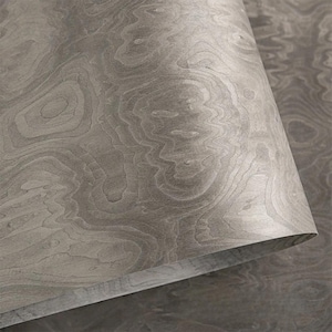 May include: Close-up of a rolled sheet of gray wood veneer. The wood grain pattern features swirling, organic lines and variations in tone, creating a natural, textured appearance. The edge of the rolled sheet reveals the thinness of the material.