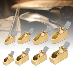 Può includere: Una collezione di piccole pialle per la lavorazione del legno color ottone con lame argentate. Ogni pialla ha un corpo rettangolare e una manopola di regolazione circolare. Le pialle sono disposte in file, suggerendo un set di strumenti per la lavorazione del legno di precisione.