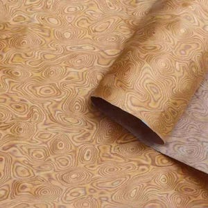 May include: A roll of wood veneer with a distinctive, swirling grain pattern in shades of tan and brown. The veneer is partially unrolled, revealing the interior. The overall effect is reminiscent of a topographic map.