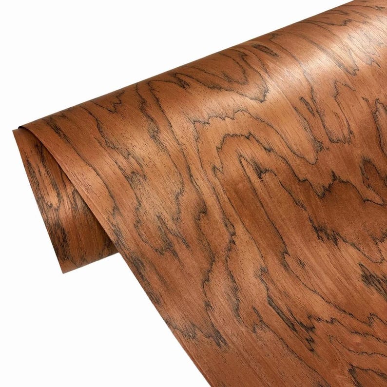 K&ouml;nnte beinhalten: Eine Rolle Holzfurnier mit einem satten, rotbraunen Farbton und dunklen, wellenf&ouml;rmigen Maserungsmustern. Das Holz hat eine glatte, gl&auml;nzende Oberfl&auml;che. Dieses Furnier eignet sich f&uuml;r Holzbearbeitungs- und Bastelprojekte.