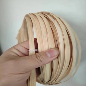 May include: A bundle of thin, light-colored bamboo strips, held together with white plastic ties. The strips are tightly wound, creating a circular shape. The natural wood grain is visible.