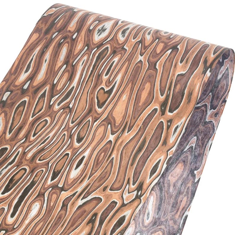 Puede incluir: Un rollo de papel con un dise&ntilde;o de vetas de madera. El dise&ntilde;o presenta l&iacute;neas onduladas en tonos marr&oacute;n, beige y blanco, creando un aspecto natural y org&aacute;nico. El papel est&aacute; enrollado, mostrando el patr&oacute;n en la superficie.
