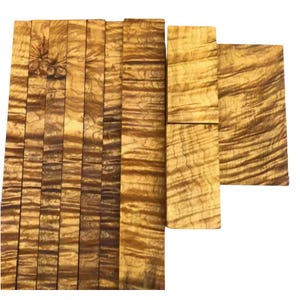 May include: A selection of rectangular wooden pieces with a unique grain. The wood displays a warm, golden-brown colour with darker brown streaks, creating a visually appealing texture. The pieces are arranged together, showcasing the natural beauty of the wood.