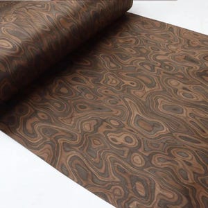 May include: A rolled sheet of wood veneer displaying a swirling, organic pattern in shades of brown and dark grey. The wood grain creates a natural, flowing design, suitable for furniture making or decorative projects.