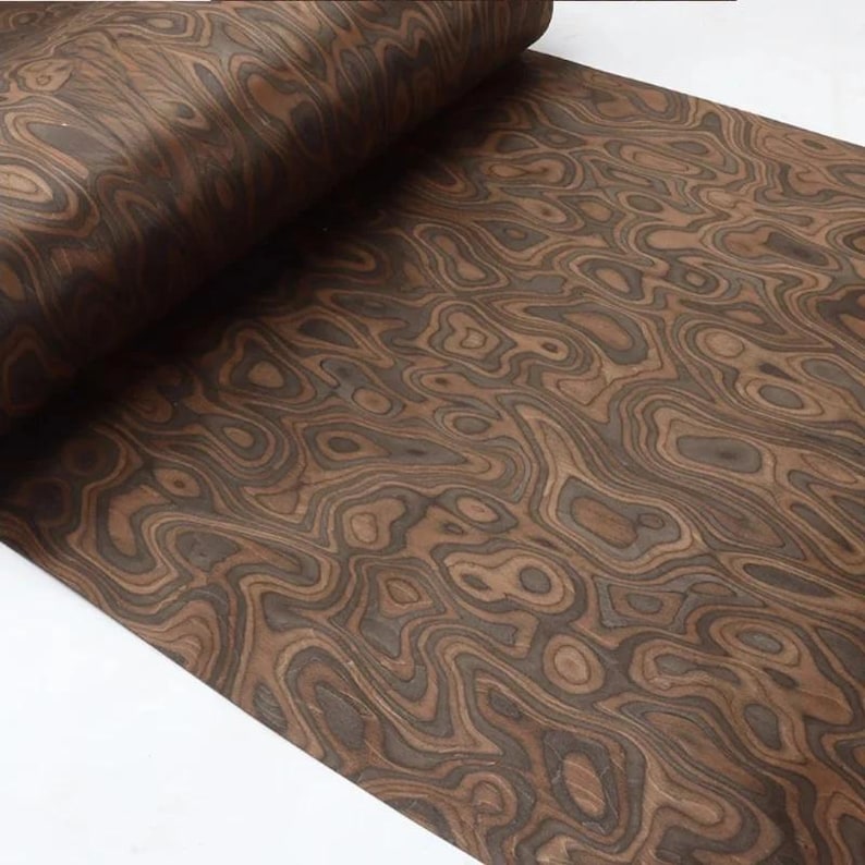 May include: A rolled sheet of wood veneer displaying a swirling, organic pattern in shades of brown and dark grey. The wood grain creates a natural, flowing design, suitable for furniture making or decorative projects.