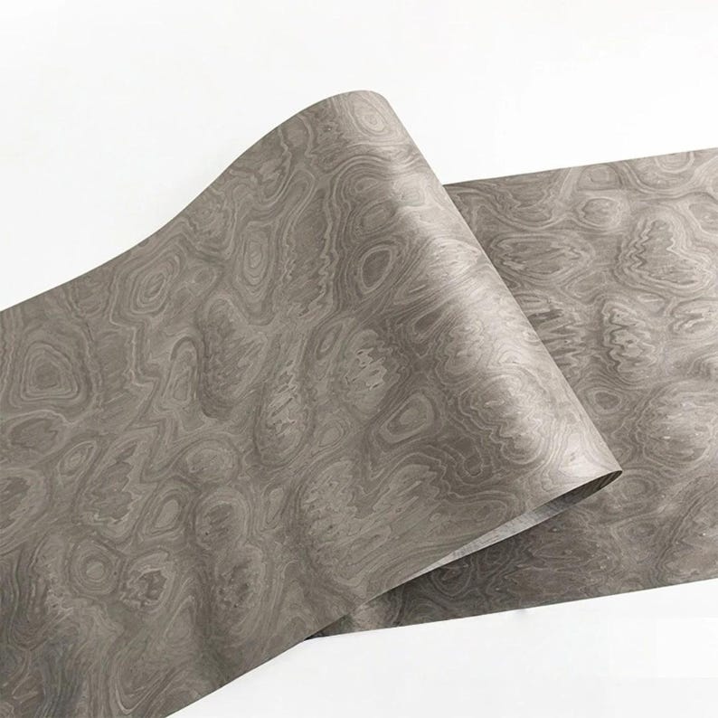 May include: A roll of gray decorative paper with a wood grain pattern. The paper is curled, revealing the intricate swirling design. The paper has a matte finish and is suitable for crafts and decorative projects.