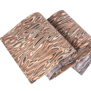 Puede incluir: Dos rollos de papel decorativo con un patr&oacute;n de vetas de madera. El papel presenta una mezcla de tonos marr&oacute;n, beige y negro, creando una apariencia naturalista y org&aacute;nica. Los rollos est&aacute;n ligeramente angulados, mostrando el flujo del patr&oacute;n.