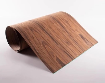 May include: A rolled sheet of wood veneer with a rich, brown grain pattern. The veneer is curled, revealing the underside with a green edge. The wood grain features dark and light brown streaks.