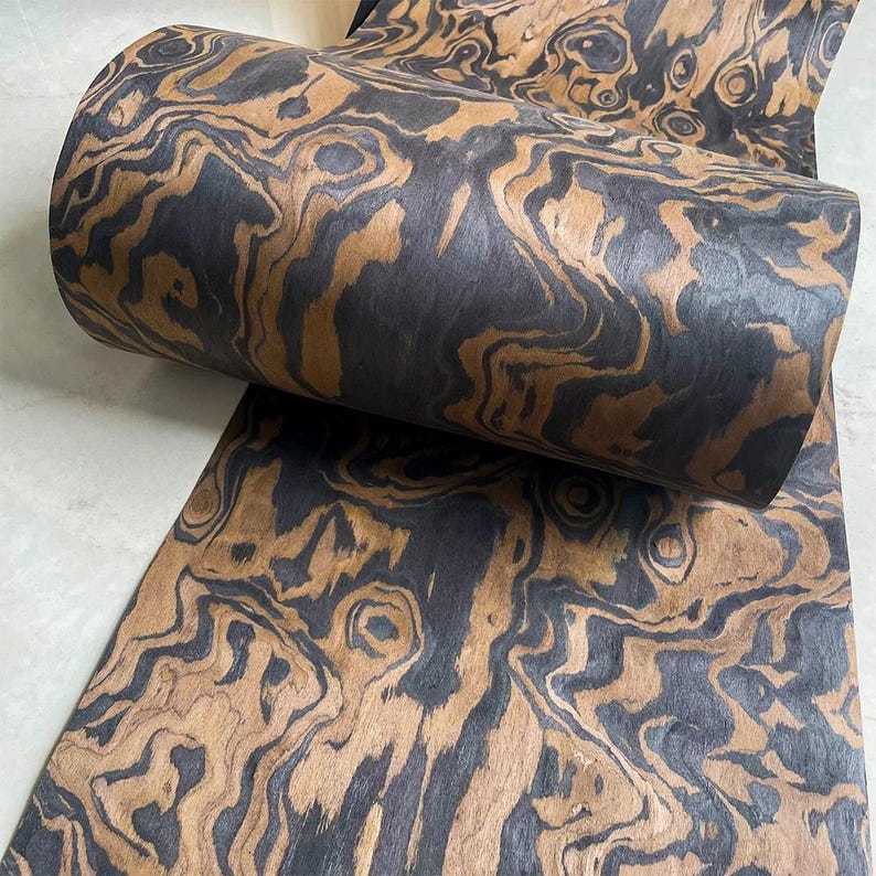 May include: A roll of decorative paper with a swirling pattern in shades of brown and black. The paper has a wood grain appearance, with dark and light areas creating a marbled effect. The paper is partially rolled, revealing the pattern.