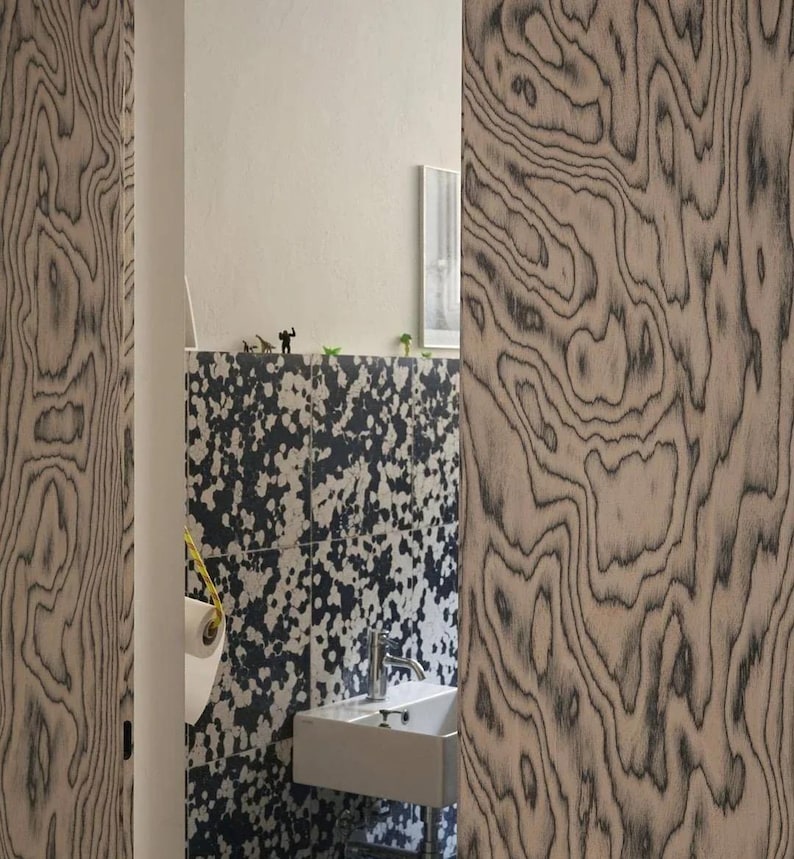 Puede incluir: Interior de ba&ntilde;o con dise&ntilde;o moderno. Las paredes presentan un llamativo patr&oacute;n moteado en blanco y negro, complementado con paneles de madera con una veta &uacute;nica. Se ven un lavabo blanco y un rollo de papel higi&eacute;nico.