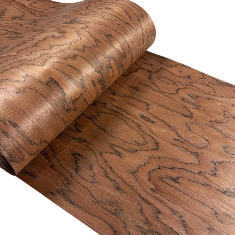 K&ouml;nnte beinhalten: Eine gerollte Holzfurnierplatte mit einem warmen, rotbraunen Farbton und dunklen, wirbelnden Maserungsmustern. Das Holz hat eine glatte, polierte Oberfl&auml;che, die ihm ein nat&uuml;rliches, organisches Aussehen verleiht. Das Furnier ist wahrscheinlich f&uuml;r M&ouml;bel oder Dekorationszwecke bestimmt.
