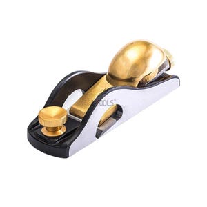 May include: A compact block plane with a black base, silver blade, and brass fittings. The plane has a rounded brass knob and a brass lever cap. The blade is visible at the front. This hand tool is designed for woodworking and is approximately 15 cm in length.