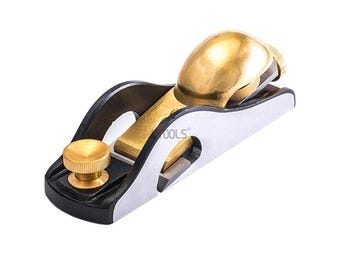 May include: A small, hand-held block plane with a black base, silver blade, and brass hardware. The plane features a rounded brass knob and a brass lever cap. The blade is visible at the front of the plane. The tool is designed for woodworking.