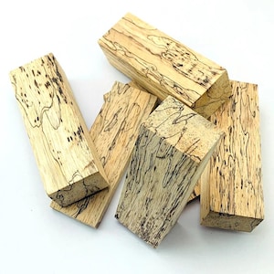 May include: A collection of light-colored wood blocks with striking black veining patterns. The blocks are rectangular and vary in size, showcasing the natural grain and unique markings of the wood. The arrangement highlights the natural beauty of the wood.