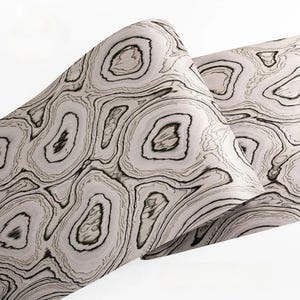 May include: Two decorative pillows with a unique, abstract pattern. The design features concentric, organic shapes in shades of gray and black, resembling wood grain or geological formations. The pillows have a soft, inviting appearance.