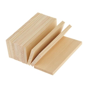 Puede incluir: Una pila de bloques de madera rectangulares de color claro con patrones de veta visibles. Los bloques están dispuestos en un grupo vertical con varias piezas de pie y una pieza colocada plana en primer plano, mostrando la textura natural de la madera.