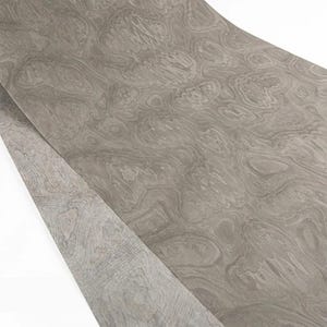 May include: A sheet of gray wood veneer with a swirling, organic grain pattern. The veneer has a light, neutral color and a smooth surface. The wood grain creates a natural, flowing design, suitable for furniture or decorative projects.