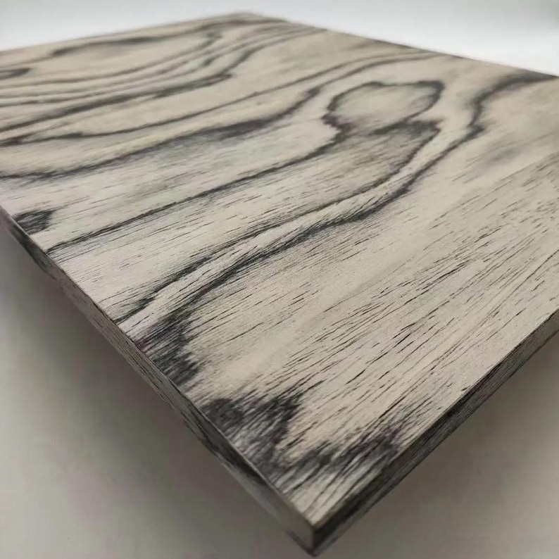 Puede incluir: Un panel de madera rectangular con una base gris claro y patrones de vetas de madera gris oscuro. La veta de la madera tiene un dise&ntilde;o natural y fluido. Los bordes del panel son visibles, mostrando el grosor de la madera.