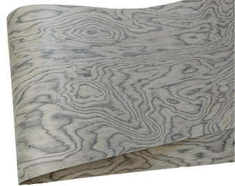 May include: A rolled sheet of wood veneer with a light gray and blue-gray wood grain pattern. The veneer has a natural, organic appearance with swirling lines and knots.