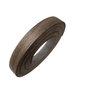May include: A roll of edge banding with a wood grain appearance. The banding is a medium brown color and appears to be made of a flexible material. The roll is tightly wound, showing the edge of the material.
