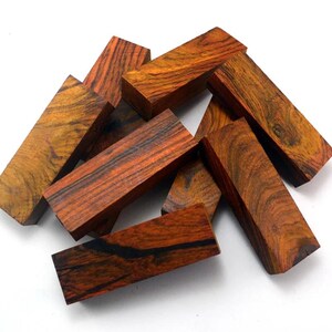 Peut inclure: Un ensemble de blocs de bois rectangulaires avec des motifs de grain riches et variés. Les blocs présentent une gamme de couleurs, allant du brun rougeâtre foncé aux teintes dorées plus claires, avec des stries sombres. Le bois semble être finement fini.
