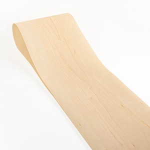 Op de afbeelding: Een gebogen stuk lichtgekleurd hout, mogelijk esdoorn, met een glad, gepolijst oppervlak. De houtnerf is zichtbaar en het stuk heeft een zachte curve, wat suggereert dat het gebruikt kan worden in meubels of houtbewerkingsprojecten.