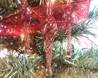 May include: Three red glass baubles with a twisted design hang on a Christmas tree. The baubles are made of clear glass with a red swirl pattern.