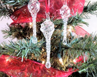 May include: Three clear glass Christmas baubles with a swirl design hanging on a Christmas tree with red ribbon.