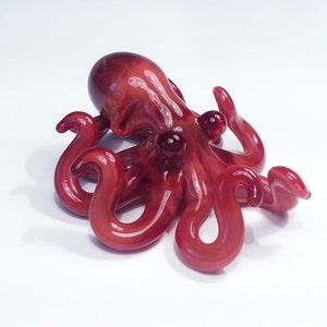 May include: A red glass octopus figurine with eight tentacles and red glass eyes. The octopus is lying on its side with its tentacles curled up.