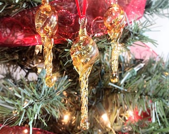 May include: Three amber glass Christmas baubles with a swirl design hanging on a Christmas tree with red ribbon.