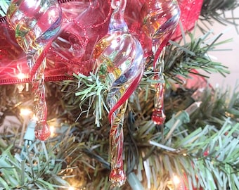 May include: Three colourful glass baubles with a swirl design hang on a Christmas tree. The baubles are red, yellow, blue, and green.
