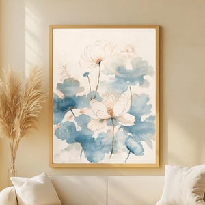 May include: Watercolor floral art print featuring large white flowers with pink centers and blue-green leaves. The artwork is framed in a light brown wooden frame. The painting has a soft, airy quality, with a focus on botanical elements.