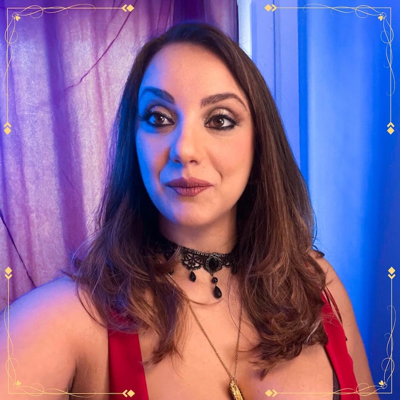 May include: A black lace choker necklace featuring a central oval pendant and small dangling black teardrop beads, worn with a thin gold chain necklace and a red garment against a purple and blue background.