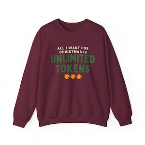 May include: A maroon sweatshirt featuring the text "ALL I WANT FOR CHRISTMAS IS UNLIMITED TOKENS" in white and green, with three orange starbursts. The casual crew neck top has long sleeves.