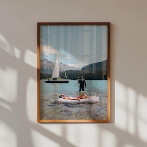 Pode incluir: Impressão artística emoldurada com uma cena surrealista. Uma pessoa flutua numa jangada insuflável num lago, com um veleiro e um garçom de fato. A obra de arte é ambientada num cenário de montanhas e água.