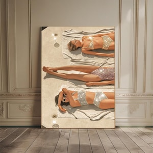 Könnte beinhalten: Gerahmter Kunstdruck mit drei Personen in glitzernden Bikinis, die auf Handtüchern sonnenbaden. Das Kunstwerk hat eine glamouröse Ästhetik mit einer neutralen Farbpalette und weicher Beleuchtung. Die Figuren sind vertikal angeordnet.