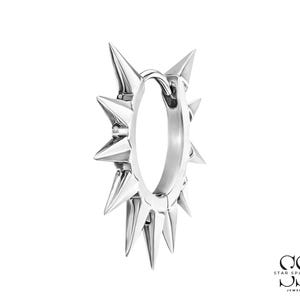 May include: A silver-toned hoop earring featuring a series of sharp, conical spikes radiating outward from the circular band. The metal has a polished, reflective finish. In the bottom right corner, the text reads STAR SPARKLE JEWELS.