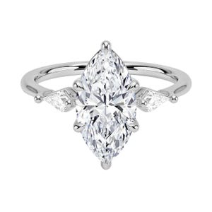 May include: A silver engagement ring featuring a large, marquise-cut diamond as the centerpiece. Two smaller pear-shaped diamonds flank the main stone. The ring has a delicate band and a classic, elegant design.