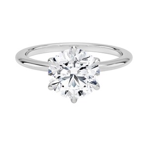Op de afbeelding: Een solitaire verlovingsring met een grote, rond geslepen diamant gezet in een gepolijste zilveren band. De diamant wordt vastgehouden door zes klauwen, die de schittering tegen een witte achtergrond benadrukken.