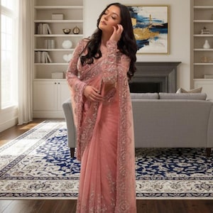 Puede incluir: Un sari rosa claro con intrincados bordados y una blusa transparente de manga larga. El sari presenta delicados adornos a lo largo de los bordes y las mangas. El texto "norzayrika" es visible en la imagen.