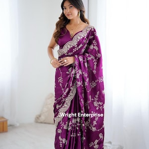 May include: A deep purple saree featuring intricate silver embroidery along the borders and scattered floral motifs throughout the fabric. The garment includes a matching sleeveless blouse with a V-neckline, showcasing detailed craftsmanship.