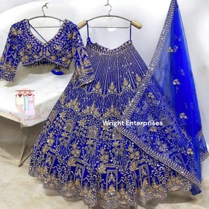 Puede incluir: Un conjunto de vestido formal bordado en azul real. El conjunto incluye una falda larga, un top corto y una bufanda transparente. La falda y el top están muy adornados con bordados y lentejuelas doradas. La bufanda tiene un borde a juego.