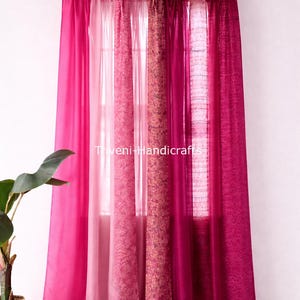 May include: A set of vibrant pink curtains hanging from a black rod. The curtains feature varying shades of pink, including a patterned panel. The text "Triveni Handicrafts" is visible on the curtains.