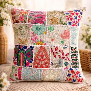 Op de afbeelding: Een vierkant patchwork kussen met een crèmekleurige achtergrond en geborduurde vierkanten in verschillende kleuren. Het kussen heeft bloemen- en paisley-ontwerpen, met de woorden "Beautiful Patchwork Pillow" bovenaan.